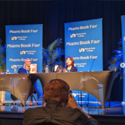 Ada Calhoun and Maud Newton, two white women, speak from behind a table on a stage at the 2022 Miami Book Fair.