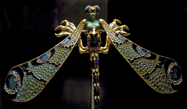 A woman's green face and bare breasts rise from a dragonfly corsage ornament of gold, enamel, chrysoprase, chalcedony, moonstones and diamonds