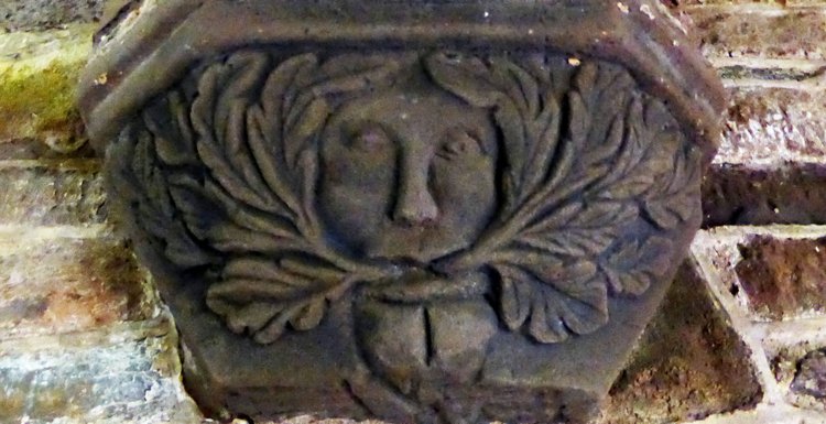 Image shows [caveat: I am not an art history person, but doing my best] what I believe to be a "disgorging" foliate head, a stone etching from Wales of a conflicted-looking man with vegetation coming out of both sides of his mouth.